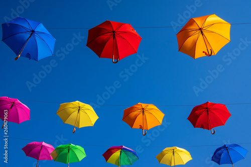 Group of umbrellas hanging on a rope isolated against blue background, wallpaper background, bright various colors scenery