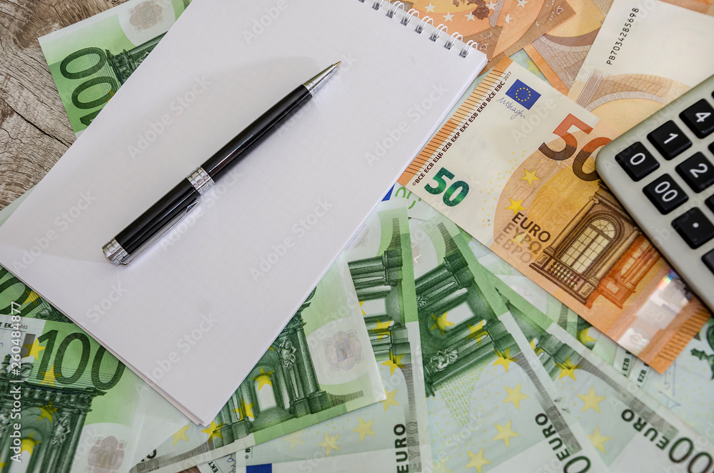 100 and 50 euros, a calculator, a notebook and a pen on a wooden background 100 and 50 euros, a calculator, a notebook and a pen on a wooden background