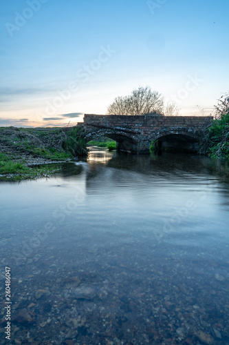 Evening reflections through arch of a brick bridge