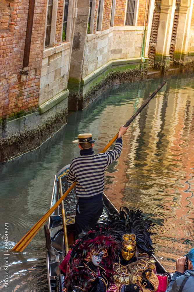 Italy, Venice, masked people ride in a gondola, and pose for photographers and tourists,
