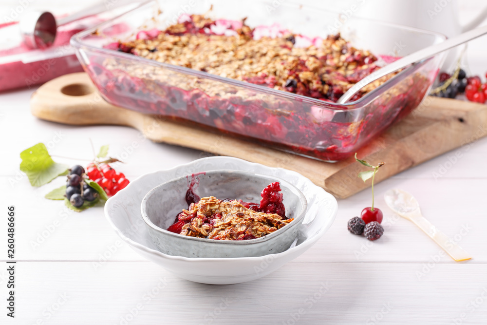 Apple and berry crumble, topped with oats in glass baking dish on white table. Crispy fruit pie, healthy summer dessert. Close-up. Apple and berry crumble, topped with oats in glass baking dish on white table. Crispy fruit pie, healthy summer dessert. Close-up.
