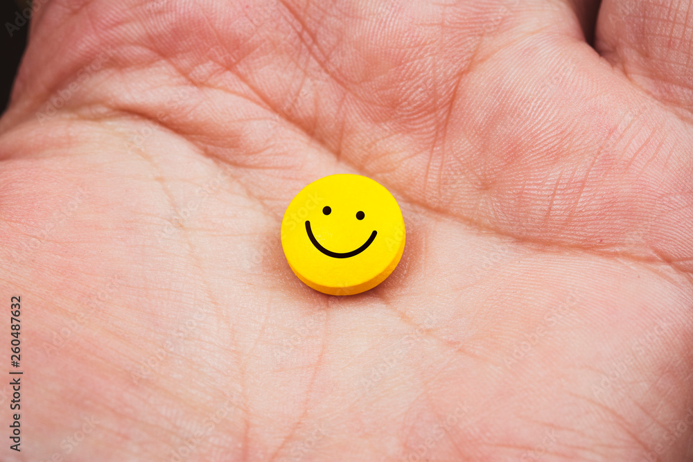 close up view of a hand holding a yellow pill with smiley face on it