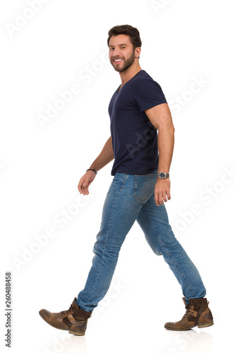 Happy Walking Man In Blue T-shirt, Jeans And Boots. Side View.
