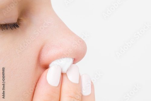Young woman fingers using cotton wool for stopping blood from nose. Isolated on light gray background. Close up. Side view. Empty place for text. 