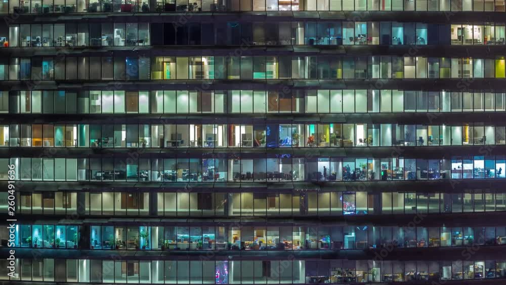 Working evening in glass office building with numerous offices with glass walls and illuminated windows timelapse. People sitting at desks. Pan right Working evening in glass office building with numerous offices with glass walls and illuminated windows timelapse. People sitting at desks. Pan right