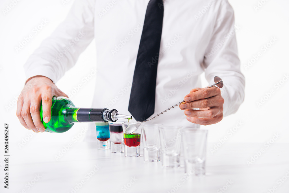 Fototapeta premium Bartender pours alcoholic drink into small glasses on bar. Colorful cocktails at the bar.