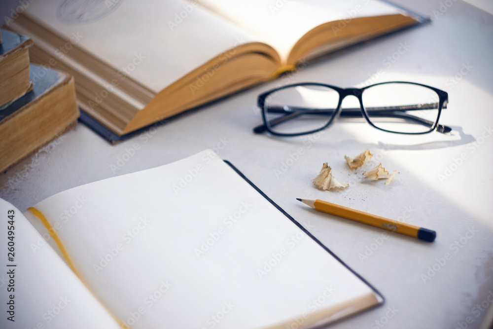 On the table are historical books and encyclopedias, open diary with a yellow bookmark, glasses, pencil and the shavings from the turning of the pencil. On the table are historical books and encyclopedias, open diary with a yellow bookmark, glasses, pencil and the shavings from the turning of the pencil.