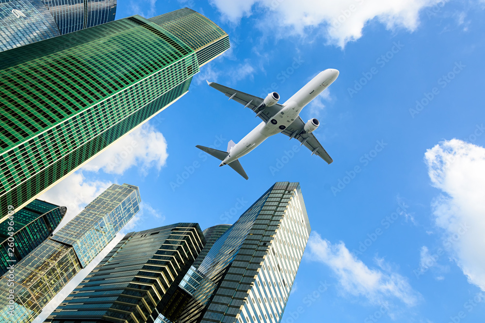 Looking up at skyscrapers in financial district of the city and airplane in the sky