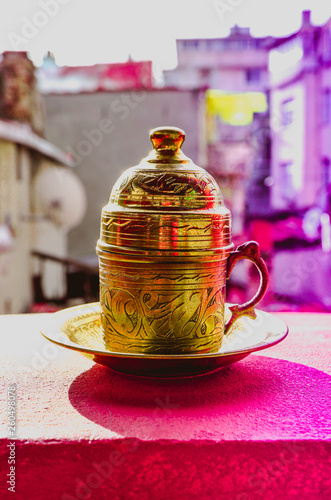 Turkish drink in a traditional golden cup. Oriental asian coffee metal tableware, blurred city on the background.