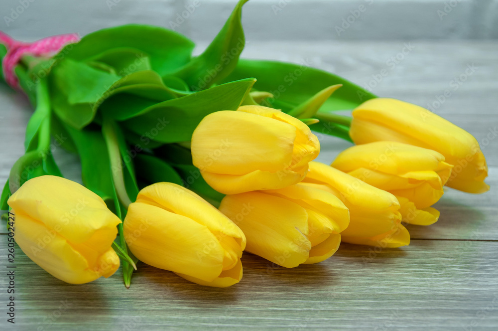 Beautiful bouquet of yellow tulips lies on a wooden gray table close up. Delicate flowers on the table. Beautiful bouquet of yellow tulips lies on a wooden gray table close up. Delicate flowers on the table.