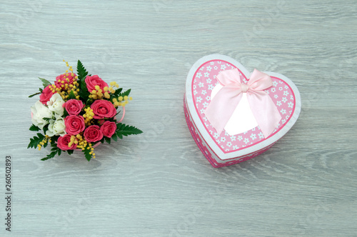 Fototapeta Naklejka Na Ścianę i Meble -  A creative bouquet of flowers with a box in the shape of a heart lies on a wooden table. Gift beloved girlfriend.