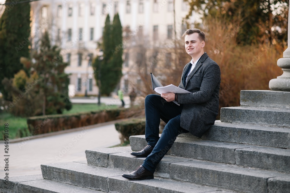 Handsome young businessman working with documents sitting on the stairs outdoor Handsome young businessman working with documents sitting on the stairs outdoor