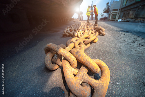 anchor chains bundle laying at bottom layer of the ship in floating dry dock, for recondition maintenance with sand blasting perform, port control and inspector surveying condition in background photo