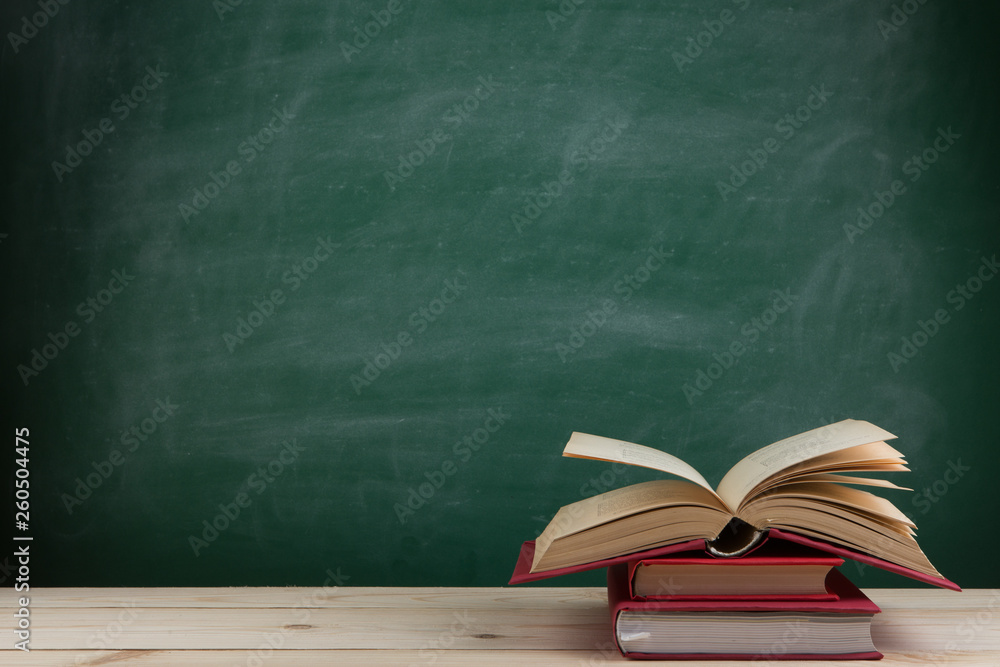 Education and reading concept - group of colorful books on the wooden table in the classroom, blackboard background Education and reading concept - group of colorful books on the wooden table in the classroom, blackboard background