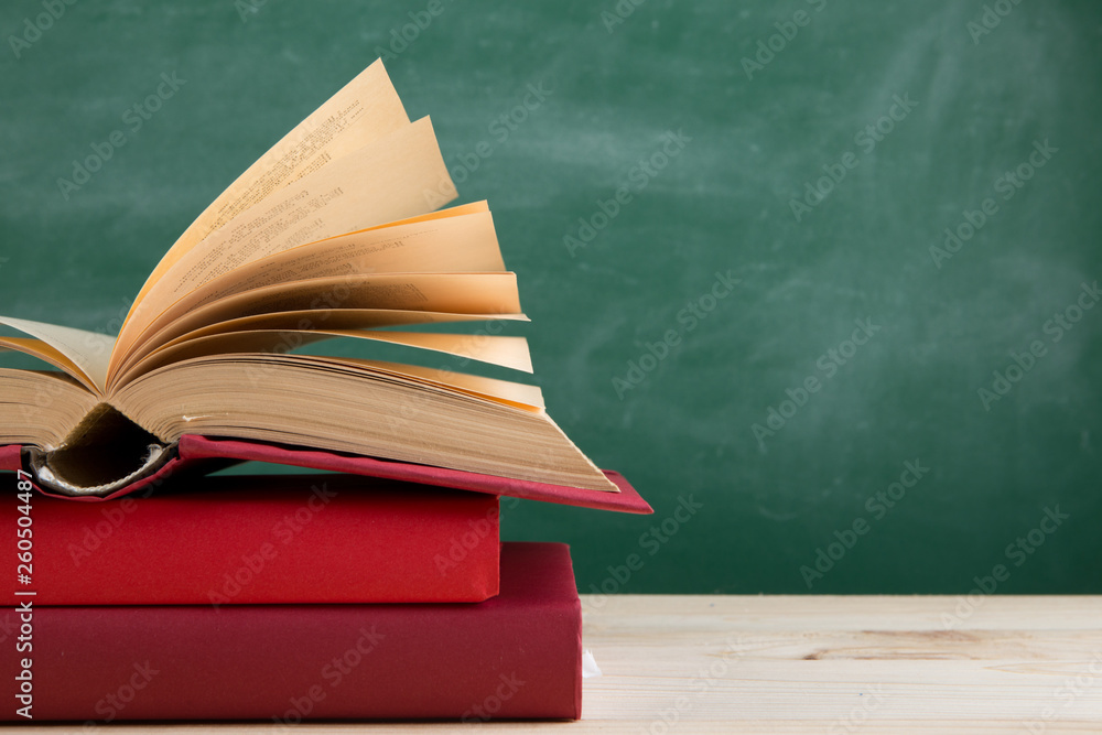 Education and reading concept - group of colorful books on the wooden table in the classroom, blackboard background Education and reading concept - group of colorful books on the wooden table in the classroom, blackboard background