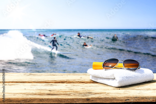 Wooden desk of free space for your decoration. Blurred background of surfers and waves . Blue ocean and white towel decoration. 
