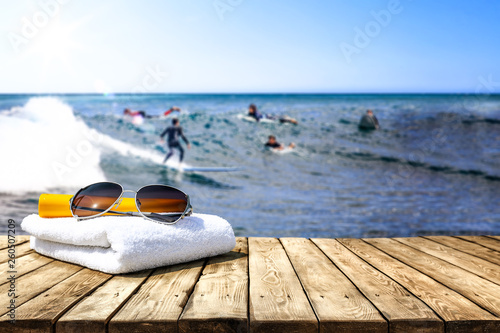 Wooden desk of free space for your decoration. Blurred background of surfers and waves . Blue ocean and white towel decoration. 