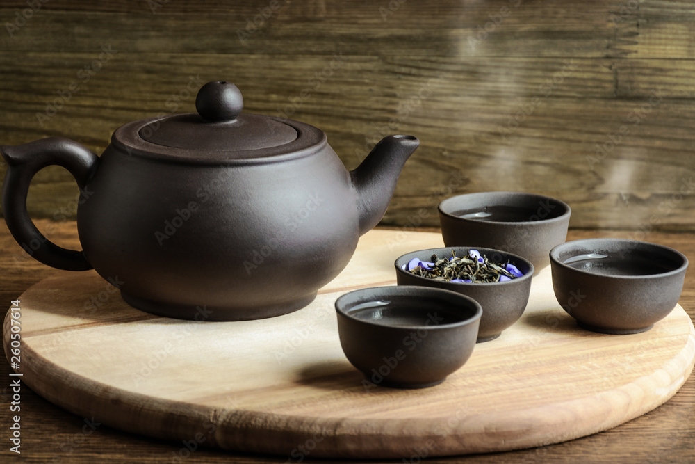 Set for tea ceremony. Large chocolate clay teapotand cups with steam, fresh green tea on wooden background. Front view. Copy space, space for text. Set for tea ceremony. Large chocolate clay teapotand cups with steam, fresh green tea on wooden background. Front view. Copy space, space for text.
