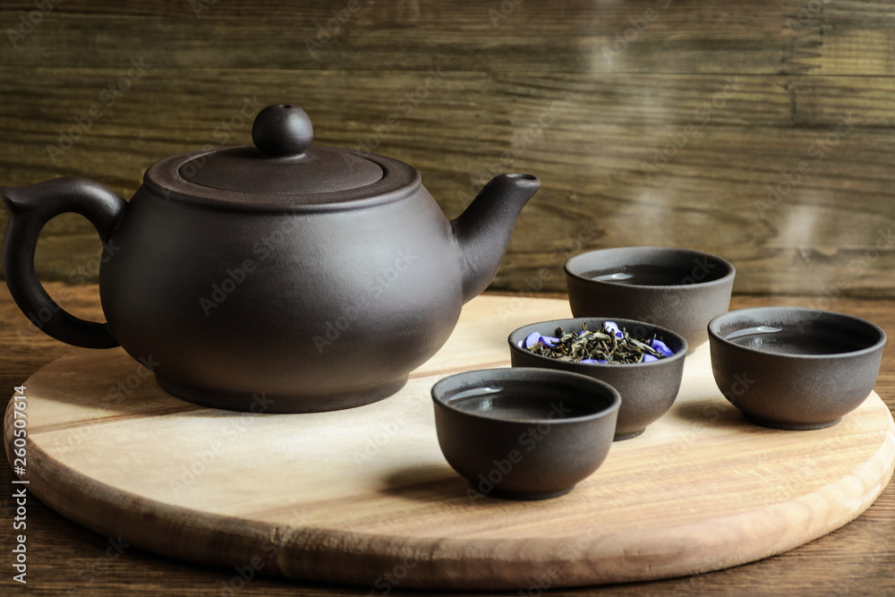 Set for tea ceremony. Large chocolate clay  teapotand cups with steam, fresh green tea on wooden background. Front view. Copy space, space for text.