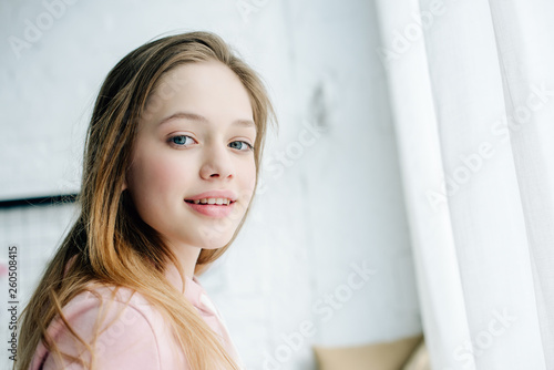 Joyful teenage kid in pink hoodie looking at camera with smile
