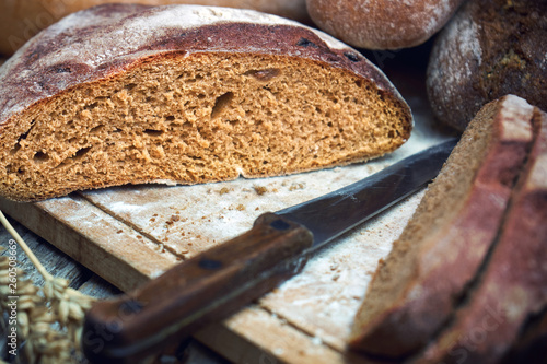 Sliced rye round bread and wheat ears with a knife on the old wooden table