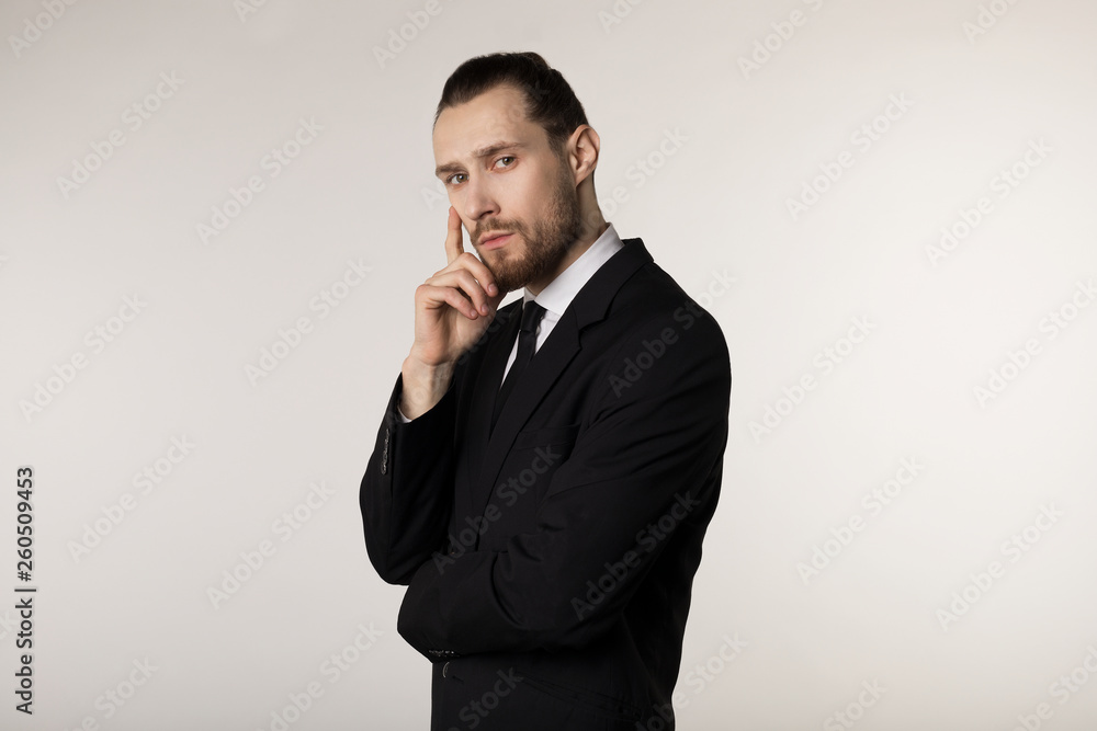 Side view portrait of attractive young businessman in black suit with stylish hairstyle holding hand on chin with thoughtful expression Side view portrait of attractive young businessman in black suit with stylish hairstyle holding hand on chin with thoughtful expression
