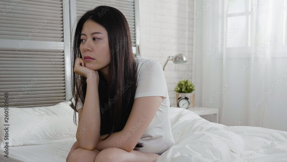Lonely young asian woman sitting on bed looking away. Depressed girl at home with sad expression. unhappy chinese female thoughtful concentrated thinking trouble problem with hand on chin in bedroom. Lonely young asian woman sitting on bed looking away. Depressed girl at home with sad expression. unhappy chinese female thoughtful concentrated thinking trouble problem with hand on chin in bedroom.