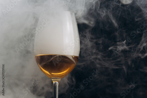 a glass of white wine on a black background. the smoke from the hookah envelops the glass. rest, holiday. alcoholic drink closeup. white fog in a glass. fog