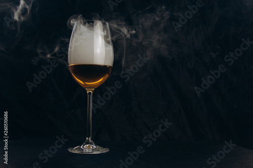 a glass of white wine on a black background. the smoke from the hookah envelops the glass. rest, holiday. alcoholic drink closeup. white fog in a glass. fog