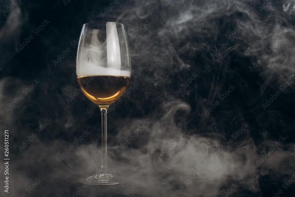 a glass of white wine on a black background. the smoke from the hookah envelops the glass. rest, holiday. alcoholic drink closeup. white fog in a glass. fog