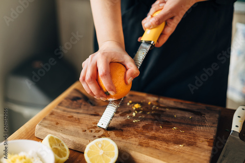 Obraz na płótnie Female chef grating orange zest on a wooden board