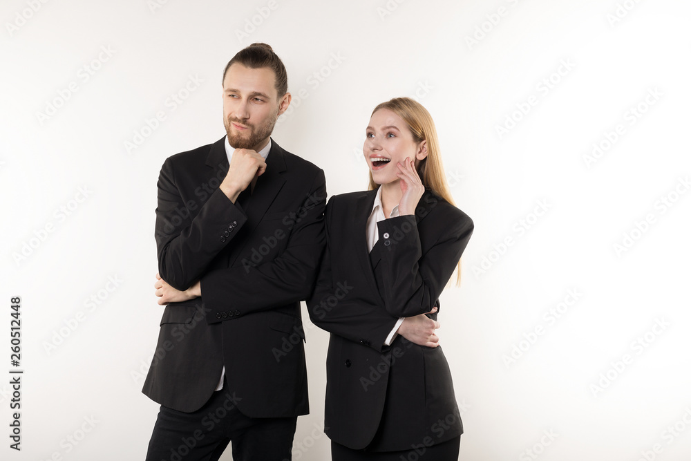 Two happy employees in black suits standing together with hands on waist looking at the presentation of their boss Two happy employees in black suits standing together with hands on waist looking at the presentation of their boss
