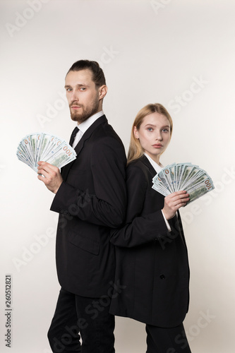 Two serious business partners handsome bearded man and beautiful blonde girl standing back to back with money in hands
