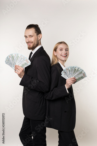 Young family couple handsome man and his beautiful blonde wife, both in black suits standing back to back with money in hands after winning the lttery
