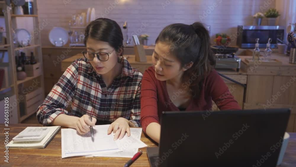 family budget finances and people concept. sisters working on kitchen table with papers and calculator counting money at home. young girls roommates enter the amount into laptop computer typing. family budget finances and people concept. sisters working on kitchen table with papers and calculator counting money at home. young girls roommates enter the amount into laptop computer typing.