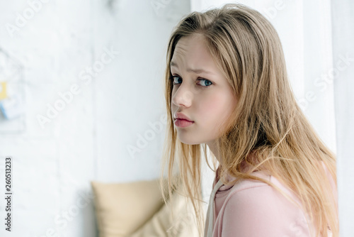 Sad teenage kid in pink hoodie looking at camera