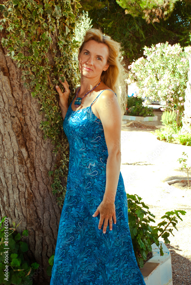 Romantic blond hair woman in blue long dress in garden with trees and jewelry. Romantic blond hair woman in blue long dress in garden with trees and jewelry.