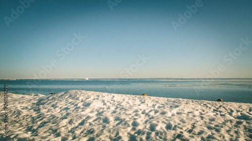 Snow pile on the beach  hill. Large snow drift isolated on a blue sky background   outdoor view of ice blocks at frozen finland lake in winter