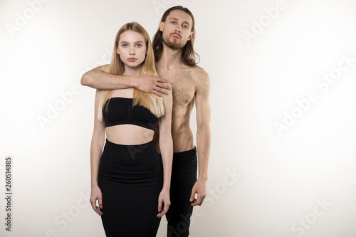 Young couple, bearded man with long hair and naked torso and beautiful girl with natural makeup hugging while posing in the studio