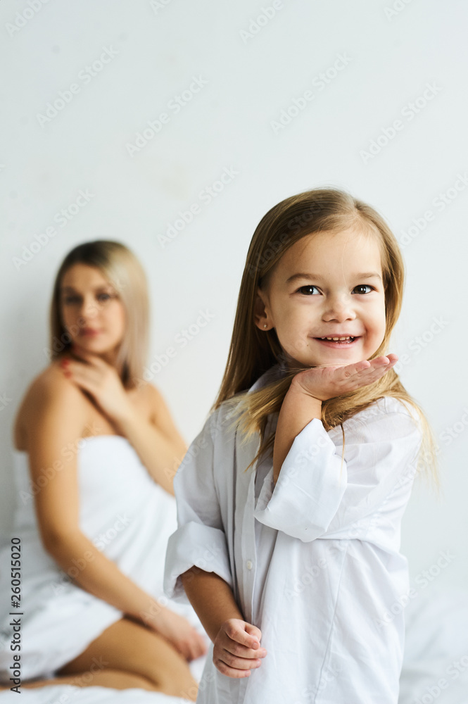 A beautiful pregnant mom and daughter playing on a white bed in the morning. A beautiful pregnant mom and daughter playing on a white bed in the morning.