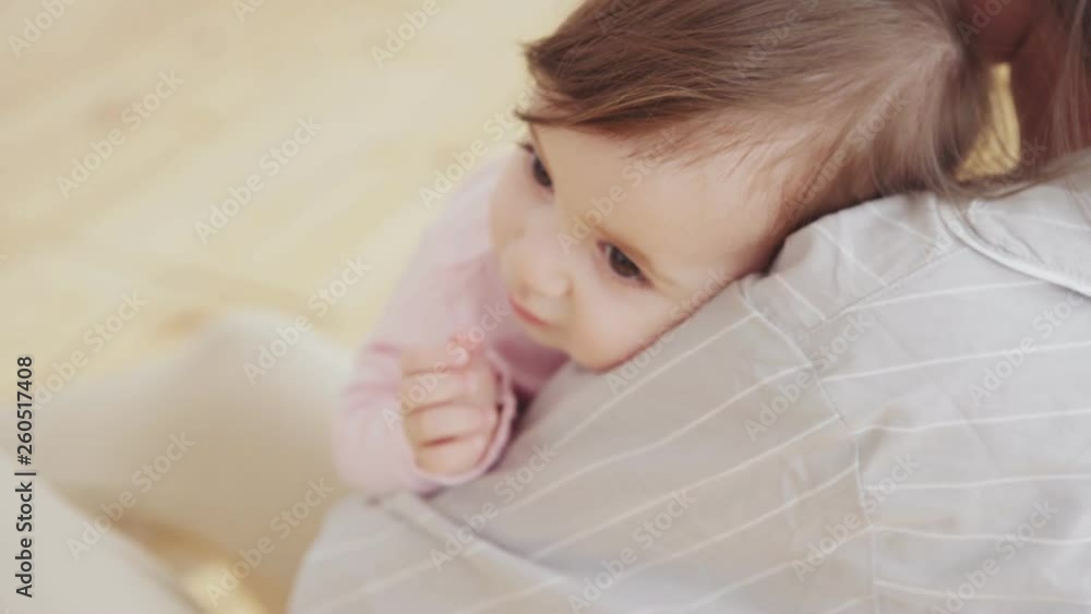 Close-up of adorable baby girl with big brown eyes lying in arms of her caring young mother trying to lull her to sleep Close-up of adorable baby girl with big brown eyes lying in arms of her caring young mother trying to lull her to sleep