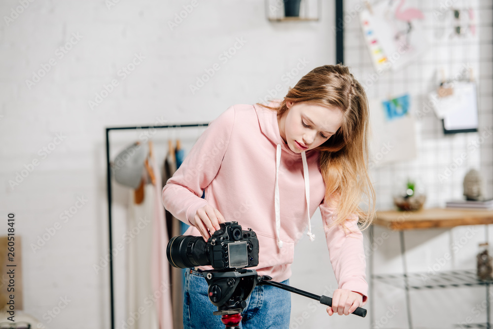 Teenage blogger in pink hoodie setting up video camera at home Teenage blogger in pink hoodie setting up video camera at home