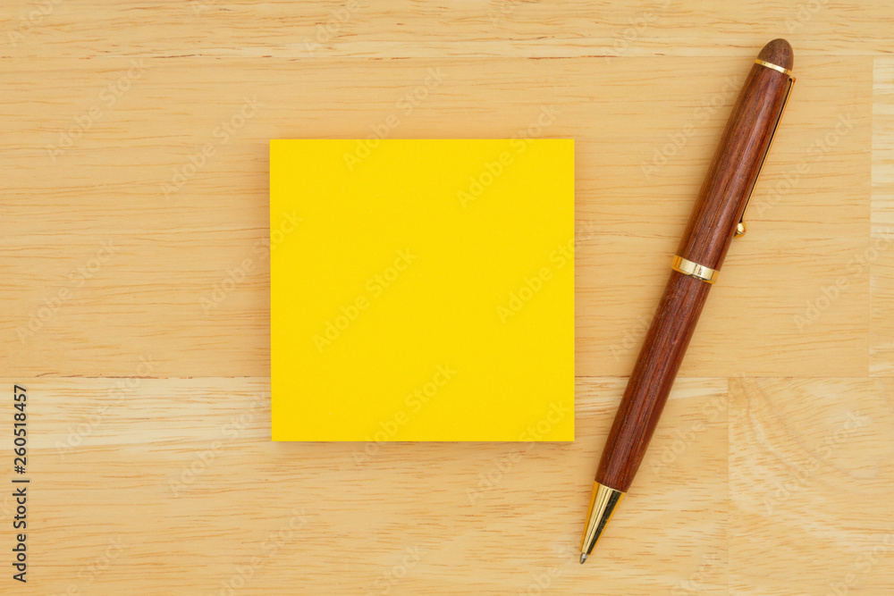 Yellow blank sticky note with a pen on textured wood background Yellow blank sticky note with a pen on textured wood background