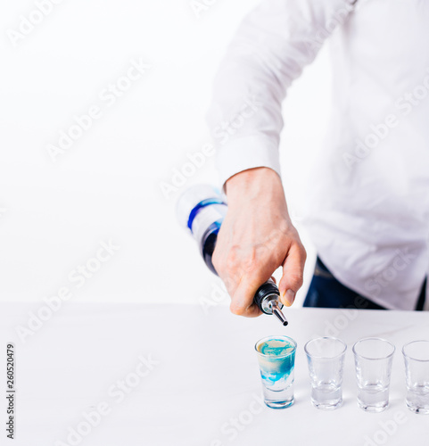 Bartender pours alcoholic drink into small glasses on bar. Colorful cocktails at the bar.