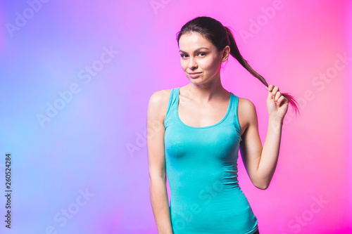 Confident sporty fit woman twirling ponytail hair lock looking at camera isolated over white studio background.