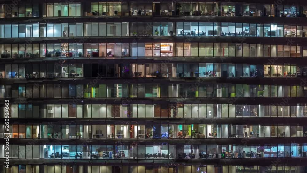 Working evening in glass business centre office building with numerous offices with glass walls and illuminated windows timelapse. People sitting at desks. Zoom in Working evening in glass business centre office building with numerous offices with glass walls and illuminated windows timelapse. People sitting at desks. Zoom in
