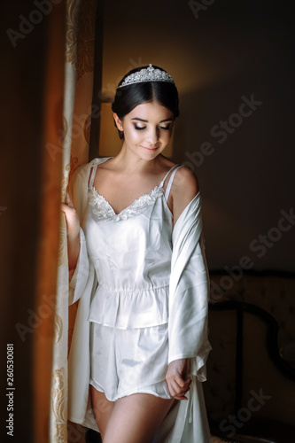 young beautiful bride posing in a robe by the window