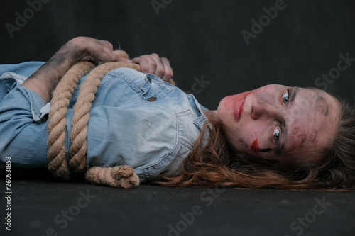 Concept portrait of offended, displeased, dirty, sharpened in captivity brunette girl on a black background, bound by a rope. Violence against women. photo