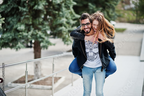 Cool multiracial couple posing with longboard. European girl jumped over shoulder arabian man.