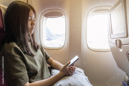 Technology while traveling on flight flying on plane with young girl passenger or woman traveller using mobile smartphone  online app and internet while sitting in airplane seat during journey